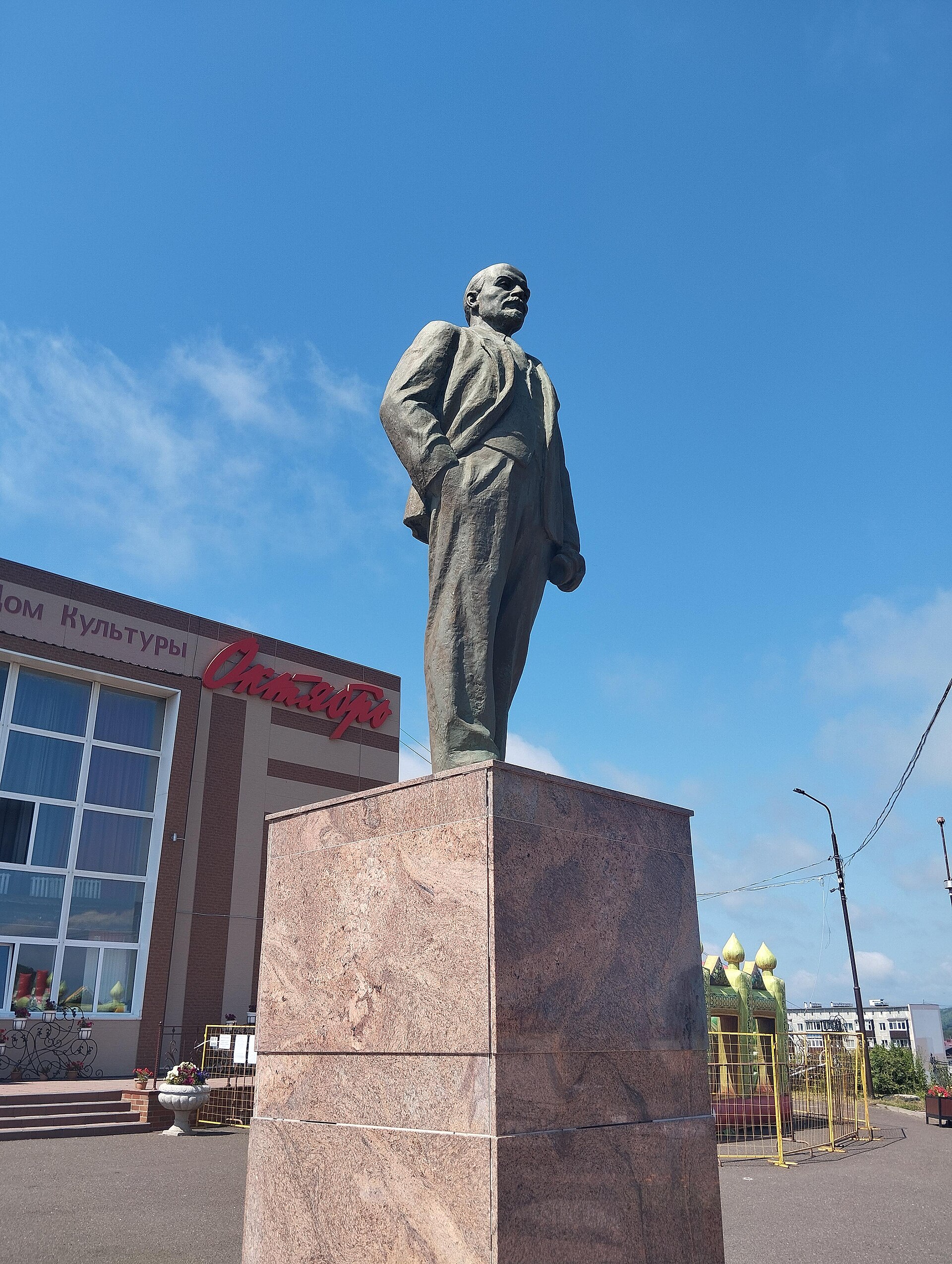 Low-angle view of a large standing statue against a clear blue sky, with a civic building below