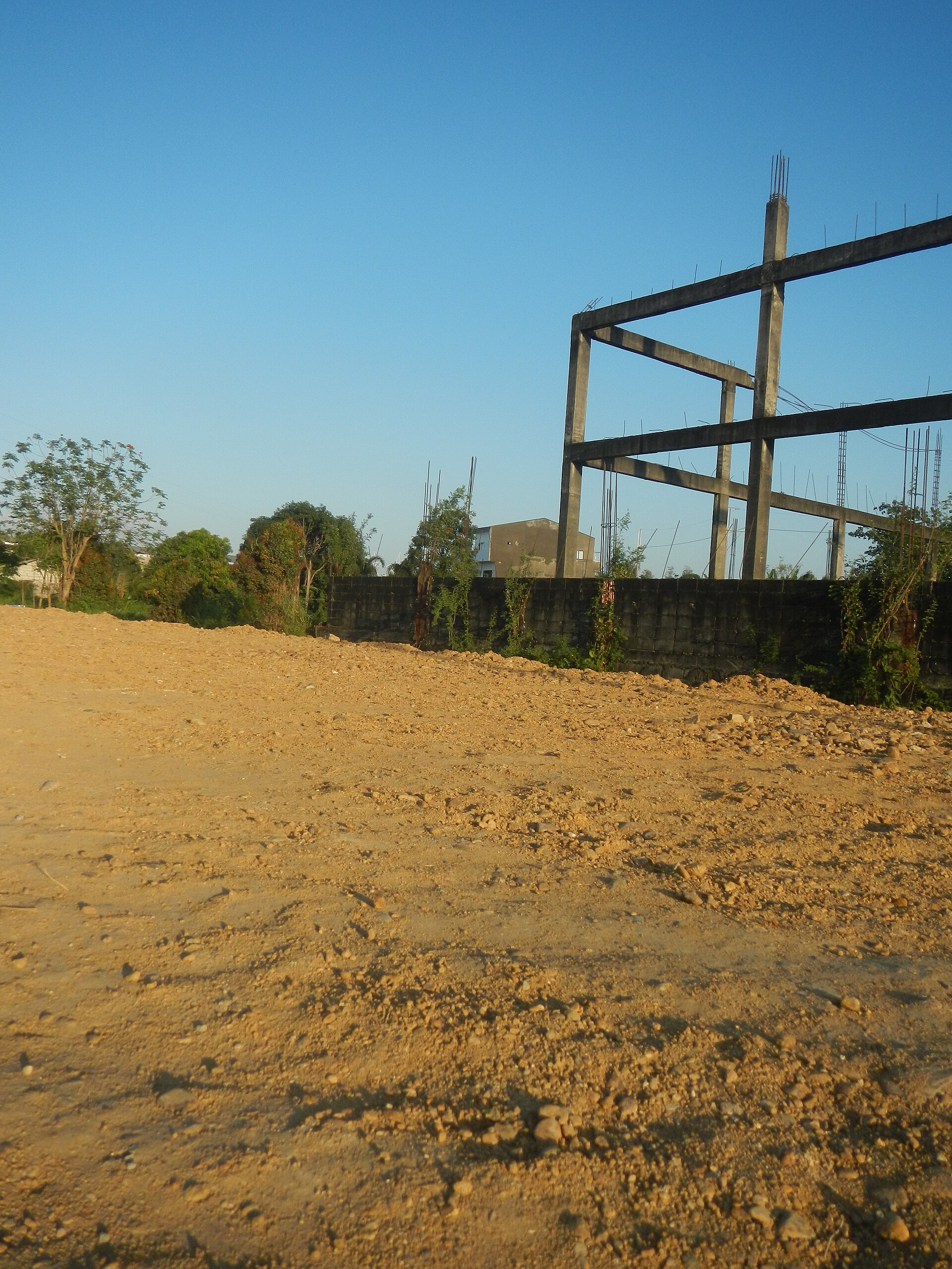 Unfinished concrete building frame beside a rough dirt road under an expansive blue sky
